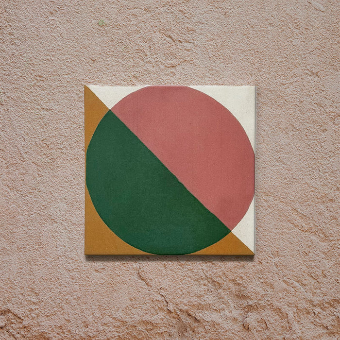 Single tile image showing the Geometry Paloma 20x20cm geometric patterned tile with pink and green semicircles and mustard and cream corner details, photographed against a textured stone background.
