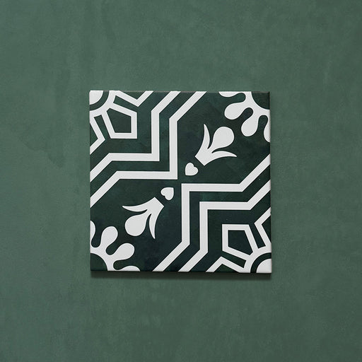 Single Brompton Victorian Green 20x20cm geometric patterned ceramic tile featuring a white floral and star motif on a deep green background, shown against a matching green backdrop in a close-up view.