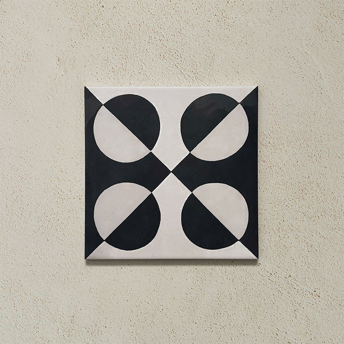 Single tile image showing the Geometry Illusion Noir 20x20cm geometric patterned tile with black and cream semicircles arranged in a bold symmetrical motif, photographed against a textured neutral background.