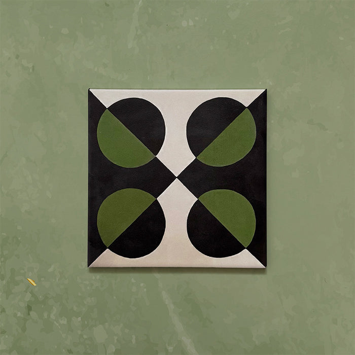 Single tile image showing the Geometry Illusion Verde Noir 20x20cm geometric patterned tile with green and black semicircles and cream corner details, photographed against a soft mottled green background.