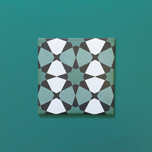 Single Agraba Verde 20x20cm Moroccan-style ceramic tile with a geometric star pattern in deep green, mint, and white tones, displayed on a teal background to highlight its intricate artisan design.