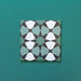 Single Agraba Verde 20x20cm Moroccan-style ceramic tile with a geometric star pattern in deep green, mint, and white tones, displayed on a teal background to highlight its intricate artisan design.