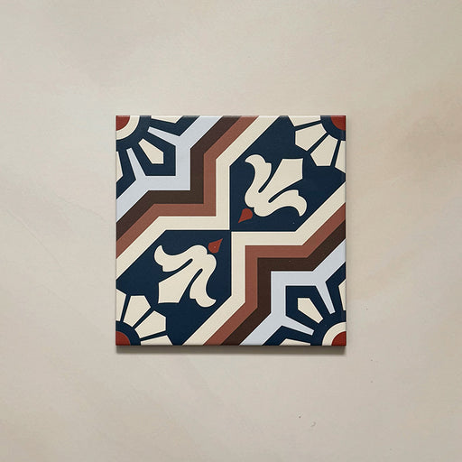 Single Brompton Grand 20x20cm Victorian-Moroccan-style ceramic tile featuring an intricate geometric and floral pattern in navy blue, terracotta, cream, and white tones, shown against a light beige background in a close-up view.