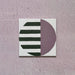 Single tile image showing the Geometry Seritina 20x20cm patterned tile with green horizontal stripes and a mauve semicircle on a cream base, photographed against a textured pink background.
