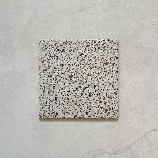 Flatlay featuring a single Dino Terrazzo Blanco Dots 20x20cm terrazzo-style ceramic tile, showcasing a white base with multicoloured stone speckles.
