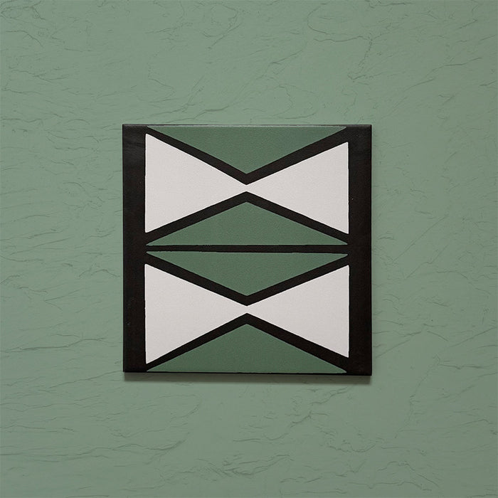 Single tile image showing the Geometry Hourglass 20x20cm patterned tile with alternating green and cream hourglass shapes outlined in charcoal, photographed against a textured sage-green background.