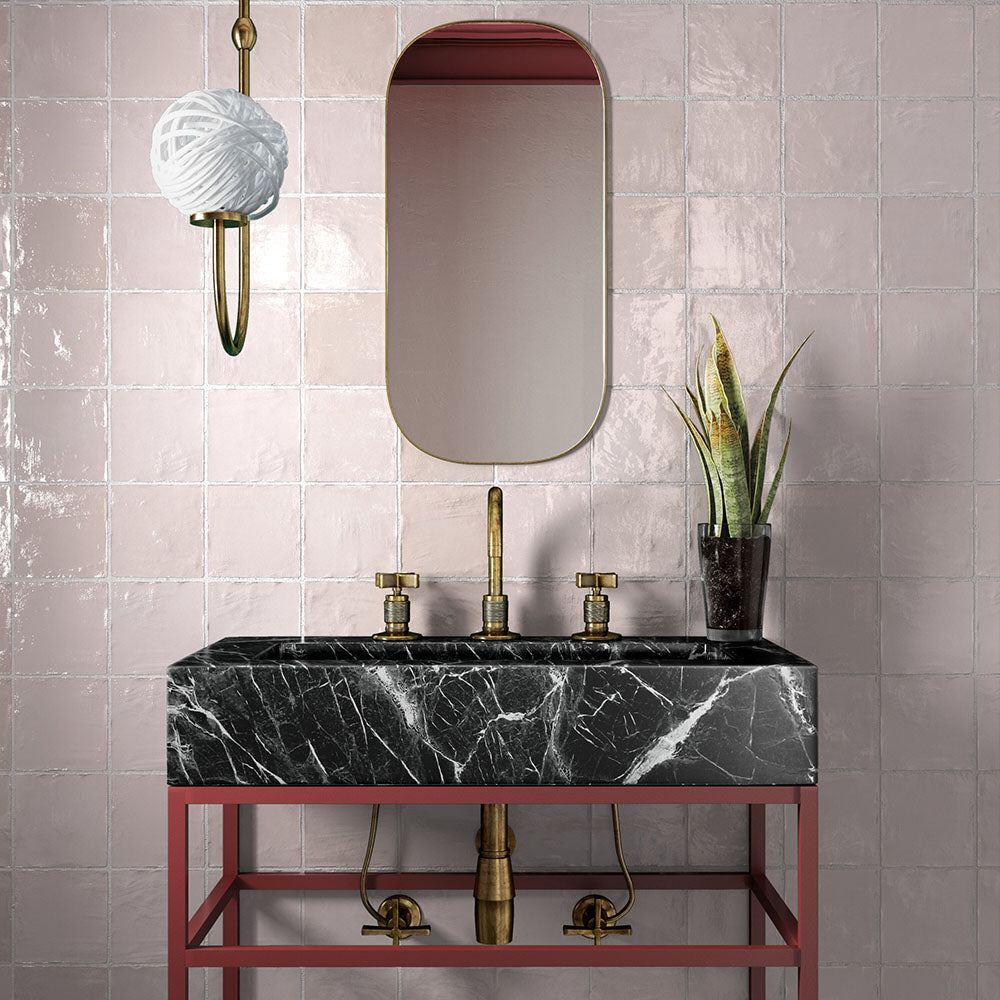 Bathroom sink setting featuring Zellij Pink Mist square Moroccan-style tiles, 13.2cm x 13.2cm, with soft blush pink tones, glossy glazed finish, subtle handmade variation, paired with a black marble basin, brass fixtures, and a warm contemporary vanity.