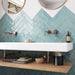 Madison Aquamarine Brick Wall Tiles 6x24.6cm — featured in a striking sink setting, these glossy teal tiles bring a fresh, ocean-inspired energy to the space. Their handcrafted finish and herringbone layout create texture and movement, beautifully complemented by warm copper fixtures and natural wood accents.