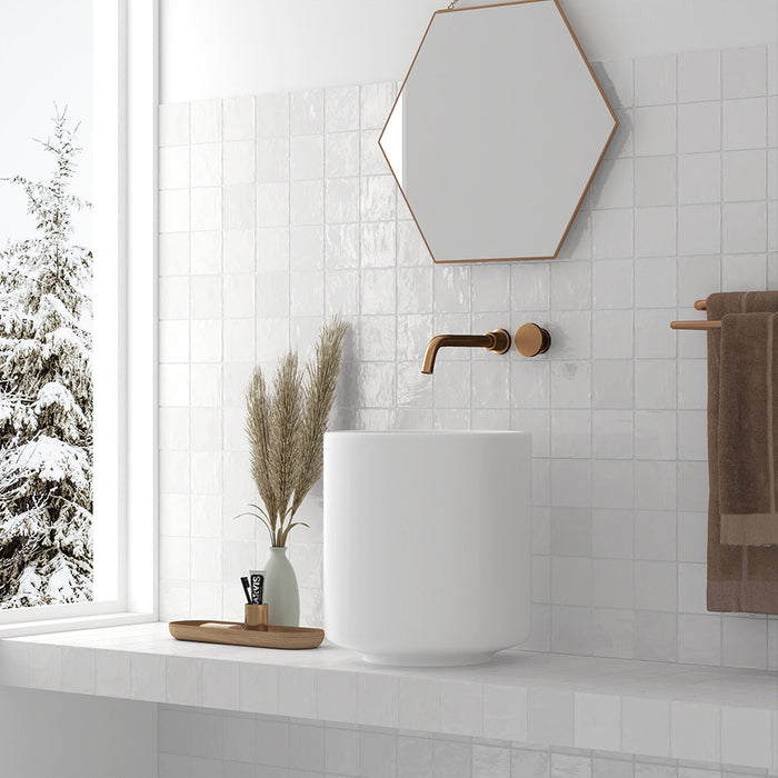 Bathroom interior featuring Zellij Oyster 10x10cm Moroccan-style square tiles in soft off-white tones, installed across walls and vanity, styled with a freestanding basin, brushed brass tap, and warm neutral accessories.