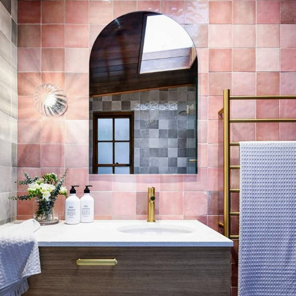 Zellij Rose Pink Square Moroccan style tiles in a 13.2cm x 13.2cm format, soft rose pink tones with a glossy finish, installed in a bathroom sink setting with a white vanity, brass tapware, arched mirror, and warm, elegant Moroccan-inspired design.