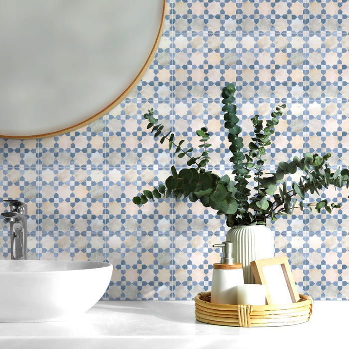 Bathroom sink area featuring Bedouin Mequinez Blue 15x15cm Moroccan-style ceramic wall tiles with a soft blue and cream geometric pattern, styled with a round mirror, eucalyptus in a ribbed vase, and natural rattan accessories.