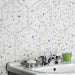 Bathroom sink setting featuring Confetti Tutti Frutti Hexagon 22×25cm terrazzo-style porcelain wall tiles with colourful multitone chips on a white base, creating a playful geometric backdrop behind a white basin with chrome fixtures.