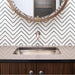 Alhambra Zig Zag Blanco 20x20cm Moroccan tiles used as a backsplash behind a sink with a brushed steel tap and round mirror, featuring a sleek black and white chevron pattern that adds a modern touch to the bathroom décor.