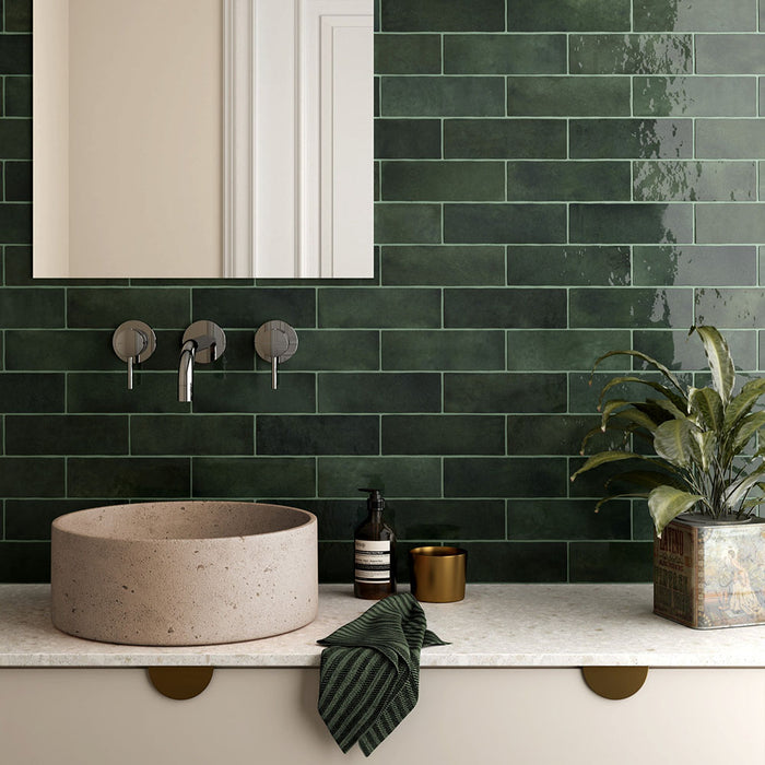 Bathroom sink setting featuring Zellij Gloss Green brick Moroccan-style wall tiles, 6.5cm x 20cm, deep green glazed finish with natural tonal variation, laid in a horizontal brick pattern behind a stone basin and brass fixtures.