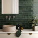 Bathroom sink setting featuring Zellij Gloss Green brick Moroccan-style wall tiles, 6.5cm x 20cm, deep green glazed finish with natural tonal variation, laid in a horizontal brick pattern behind a stone basin and brass fixtures.