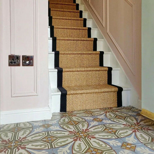 Stairway featuring Carnaby Place Victorian-style 20x20cm porcelain wall and floor tiles, showcasing an ornate floral and geometric pattern in olive, blue, red, and cream tones, styled with a natural woven stair runner and soft pink wall panelling.
