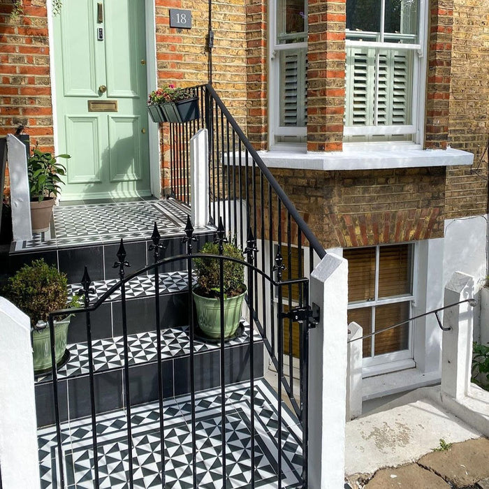 Victorian townhouse entrance featuring Sloane Square Diamonds Black and White 25x25cm ceramic floor tiles on the steps and porch, arranged in a geometric diamond pattern, styled with black railings, green potted plants, and a sage green front door.