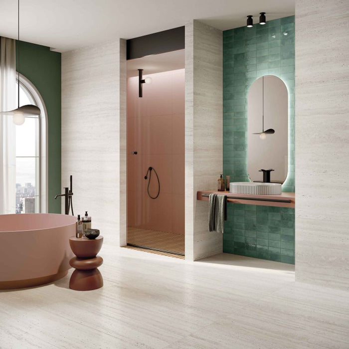 Contemporary bathroom featuring Storico Travertine Stone matt porcelain wall and floor tiles with a soft travertine effect finish, complemented by glossy green wall tiles, a blush pink freestanding bath and black fittings for a fresh, modern design.