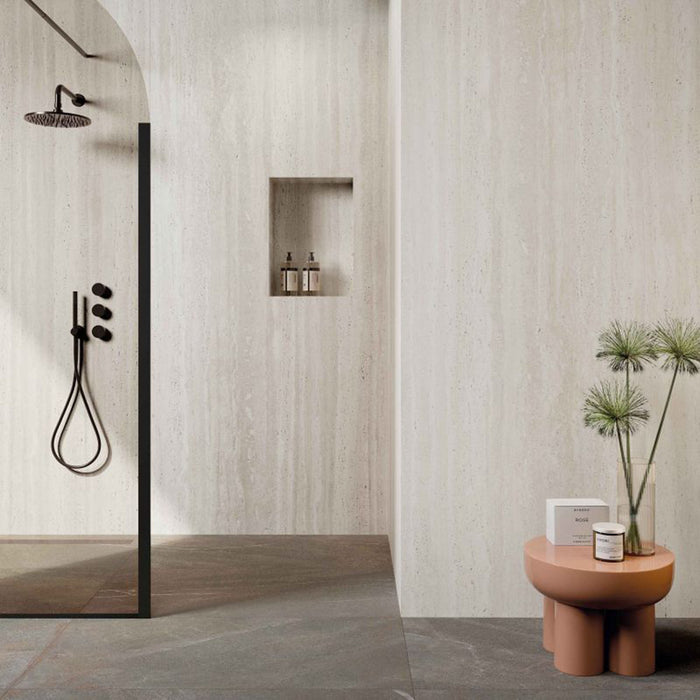 Modern bathroom featuring Storico Travertine Stone matt porcelain wall tiles with a soft travertine effect finish, paired with dark stone effect floor tiles, black shower fittings and blush pink accessories for a warm, contemporary look.