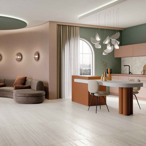 Open-plan kitchen and living space featuring Storico Travertine Stone matt porcelain floor tiles with a soft travertine effect finish, complemented by blush pink cabinetry, sage green walls and warm contemporary furnishings for a bright, elegant interior.