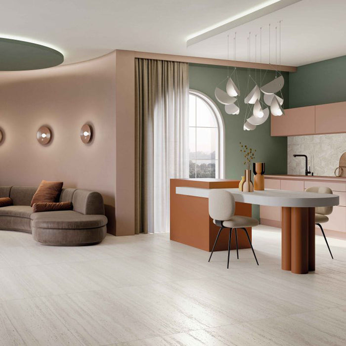 Open-plan kitchen and living space featuring Storico Travertine Stone matt porcelain floor tiles with a soft travertine effect finish, complemented by blush pink cabinetry, sage green walls and warm contemporary furnishings for a bright, elegant interior.