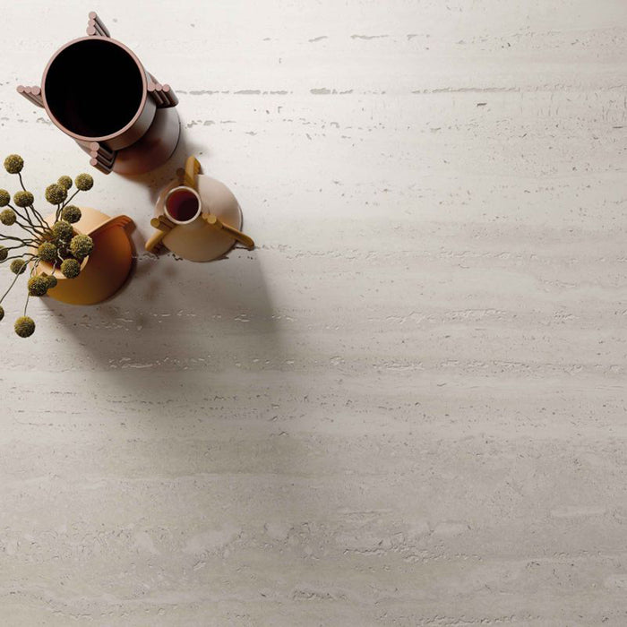Close-up of Storico Travertine Stone matt porcelain tiles showcasing a soft travertine effect surface with subtle natural veining, styled with warm-toned decorative accessories to highlight the tile's elegant, contemporary finish.