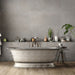 Bathroom interior featuring Tane Stone Grey Matt 30 × 60cm porcelain wall tiles, styled with a freestanding bath, vintage-style fittings, greenery, and warm wood flooring for a characterful, contemporary space.