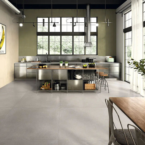 Kitchen interior featuring Tane Stone Grey Matt 60 × 60cm porcelain floor tiles, styled with industrial-style cabinetry, metal accents, a central island, and large windows for a modern, urban-inspired space.