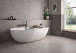 Bathroom interior featuring Tane Stone Grey Matt 60 × 60cm porcelain wall and floor tiles, styled with a freestanding bath, black fittings, soft neutral tones, and natural light for a calm, contemporary space.