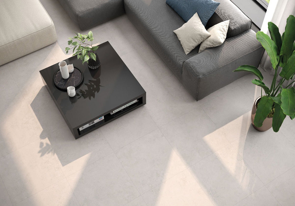 Living room featuring Tane Stone Marfil Matt 30 × 60cm porcelain floor tiles, styled with a grey sofa, black coffee table, indoor plants, and soft natural light for a clean, contemporary finish.