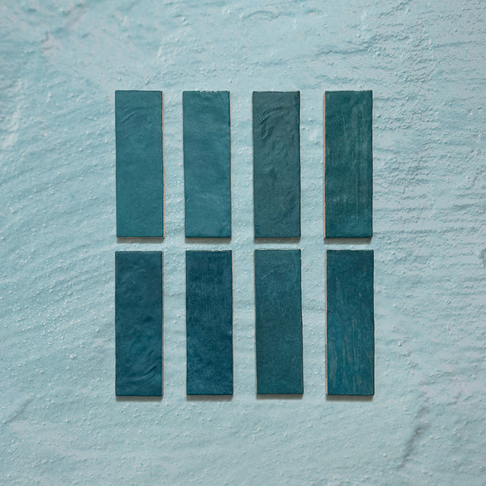 Zellij Peacock Green brick tiles, 6.5cm x 20cm, Moroccan style glazed ceramic wall tiles in rich peacock green tones with natural shade variation, glossy finish, and subtly uneven handcrafted texture, shown as individual tiles on a neutral textured background.