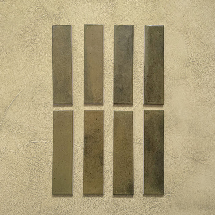 Eight Izmir Brick Daisy Green Gloss 6x25cm ceramic tiles displayed on a textured beige background, showing subtle tonal variations and a smooth reflective glaze.