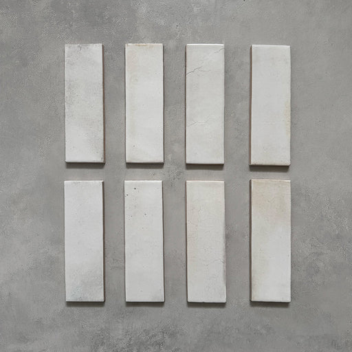 Beijing White 5.1x16.1cm Moroccan brick tiles arranged on a grey surface, showcasing their handmade texture, soft glaze variation, and natural imperfections for an authentic artisan look.