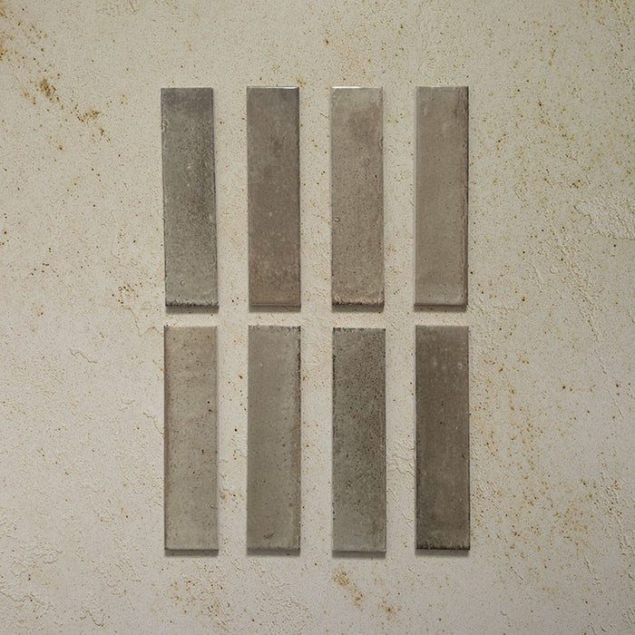 Eight Izmir Brick Sage Green Gloss 6x25cm ceramic tiles displayed on a textured beige background, showing gentle tonal variation and a soft glossy finish.