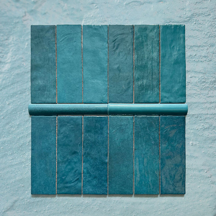 Zellij Peacock Green brick tiles with matching bullnose trim, 6.5cm x 20cm, Moroccan style glazed ceramic wall tiles in rich peacock green tones with natural colour variation, glossy finish, and softly uneven handcrafted texture, arranged as a tile and bullnose combination on a pale textured background.