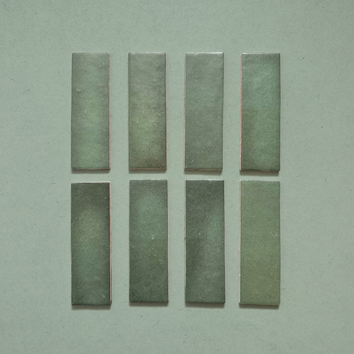 Zellij Malachite Green Brick Moroccan Style 6.5cm x 20cm glazed ceramic wall tiles in deep malachite green shades, slim brick format with subtle tonal variation, handcrafted zellige texture, glossy finish, laid out individually on a neutral background to show colour variation.