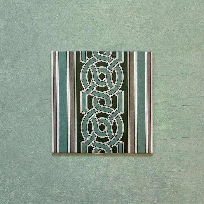Single Europa Toulouse 20x20cm Victorian Moroccan style border tile displayed against a textured green background, featuring a decorative interlocking geometric pattern in green, grey and cream tones.