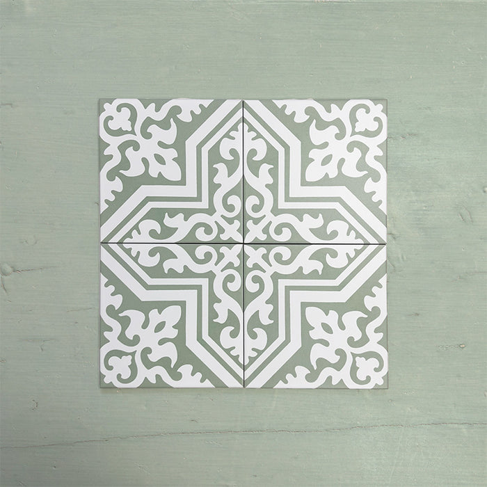 Four Europa Trondheim Sage Green 20x20cm Victorian Moroccan style tiles arranged together to showcase the repeating decorative pattern in sage green and white tones, displayed against a textured green background.