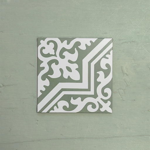 Single Europa Trondheim Sage Green 20x20cm Victorian Moroccan style tile displayed against a textured green background, featuring a decorative geometric and floral pattern in sage green and white tones in a close-up product setting.