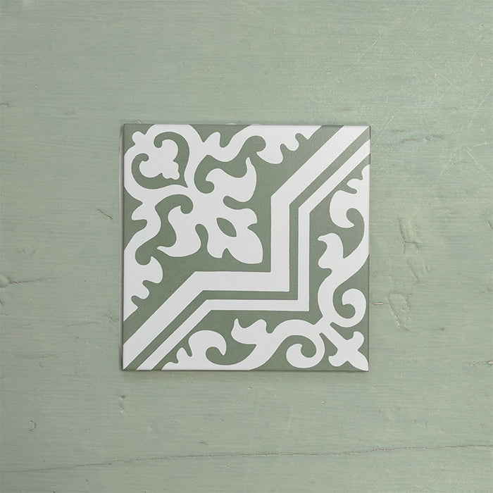 Single Europa Trondheim Sage Green 20x20cm Victorian Moroccan style tile displayed against a textured green background, featuring a decorative geometric and floral pattern in sage green and white tones in a close-up product setting.