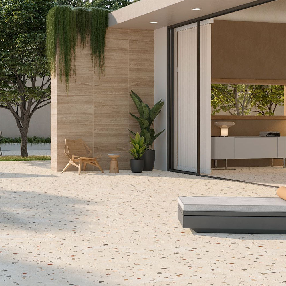 Outdoor terrace featuring Tulsa Marfil 66 × 66cm terrazzo-effect porcelain wall and floor tiles, showcasing a warm ivory base with subtle multicoloured stone fragments, paired with natural wood-effect cladding, minimalist outdoor furniture, and soft greenery for a calm, contemporary setting.
