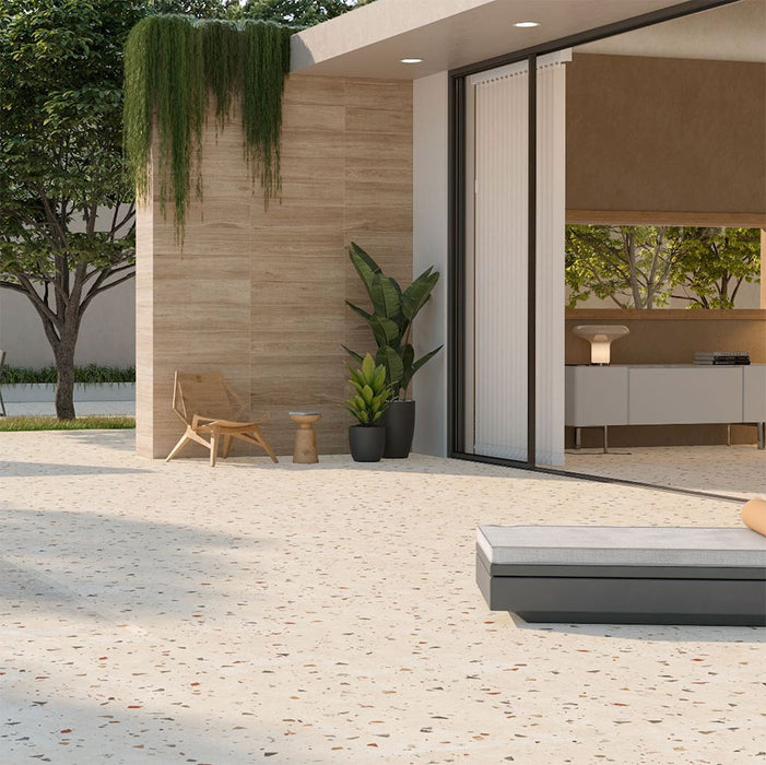 Outdoor terrace featuring Tulsa Marfil 66 × 66cm terrazzo-effect porcelain wall and floor tiles, showcasing a warm ivory base with subtle multicoloured stone fragments, paired with natural wood-effect cladding, minimalist outdoor furniture, and soft greenery for a calm, contemporary setting.