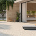Outdoor terrace featuring Tulsa Marfil 66 × 66cm terrazzo-effect porcelain wall and floor tiles, showcasing a warm ivory base with subtle multicoloured stone fragments, paired with natural wood-effect cladding, minimalist outdoor furniture, and soft greenery for a calm, contemporary setting.