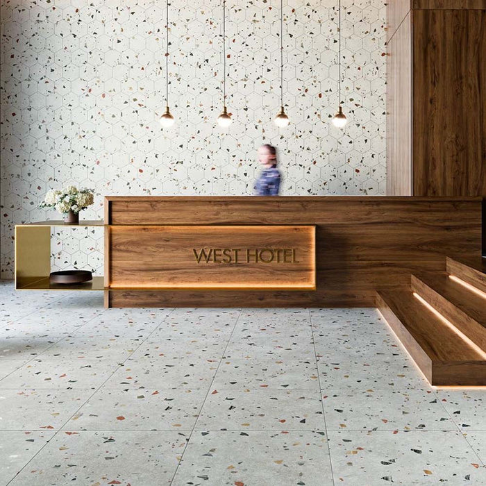 Hotel reception interior featuring Tulsa Silver Terrazzo 66 × 66cm porcelain wall and floor tiles, with a soft grey base and scattered multicoloured aggregate chips, paired with warm wood panelling and minimalist lighting for a refined, contemporary setting.