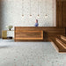 Hotel reception interior featuring Tulsa Silver Terrazzo 66 × 66cm porcelain wall and floor tiles, with a soft grey base and scattered multicoloured aggregate chips, paired with warm wood panelling and minimalist lighting for a refined, contemporary setting.