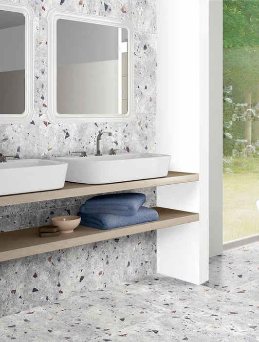 Bathroom vanity area featuring Tulsa Silver Terrazzo 66 × 66cm porcelain wall and floor tiles, with a soft grey base and multicoloured aggregate chips, paired with twin basins, light wood shelving, and clean white framing for a calm, contemporary finish.