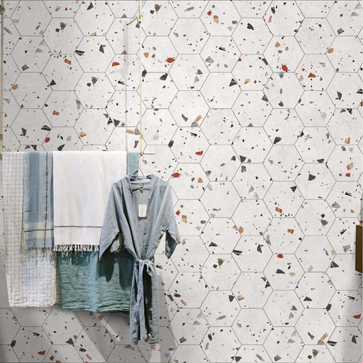 Bathroom wall featuring Tulsa White Terrazzo Hexagon 25 × 22cm porcelain tiles, with a clean white base and scattered multicoloured aggregate chips, laid in a honeycomb pattern and paired with soft textiles for a fresh, contemporary look.