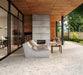 Contemporary outdoor patio featuring Venetian Ivory 2cm 60cm x 120cm terrazzo effect matt porcelain paving, with an anti-slip finish, creating a seamless terrace alongside timber cladding, concrete fireplace and modern garden seating.
