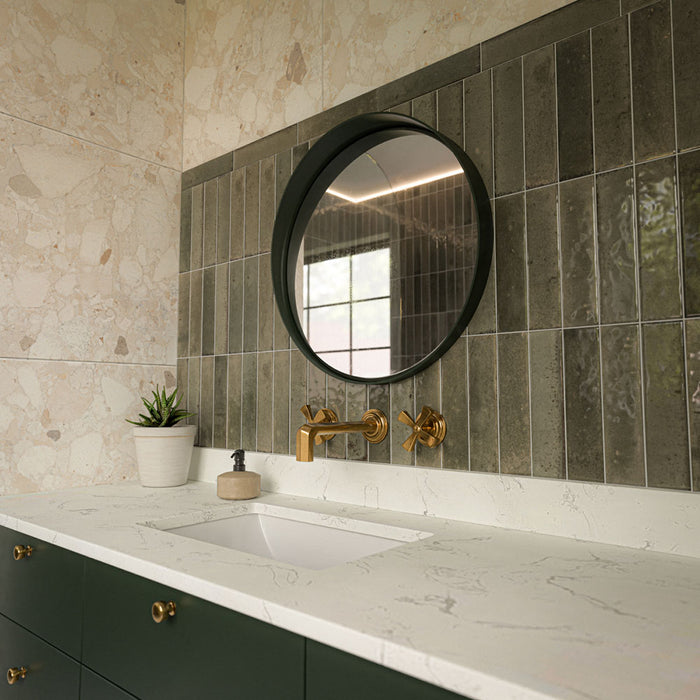 Contemporary bathroom vanity featuring Venetian Ivory terrazzo effect wall tiles, Izmir Sage Green gloss brick splashback tiles, Agraba Natural Moroccan style patterned floor tiles, a dark green floating vanity and brushed brass brassware.