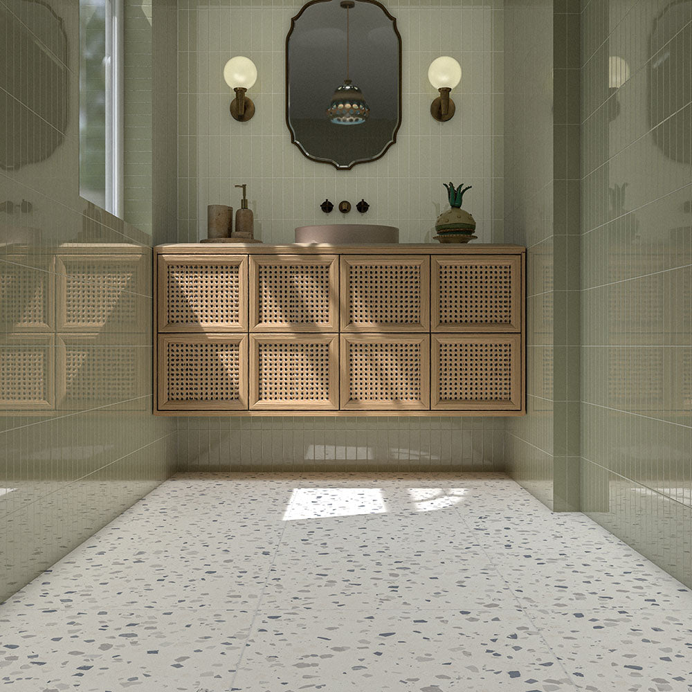 Contemporary bathroom featuring Veneto Medium White 60cm x 60cm terrazzo effect porcelain floor tiles, paired with pale green wall tiles, a wooden cane vanity and brass details.
